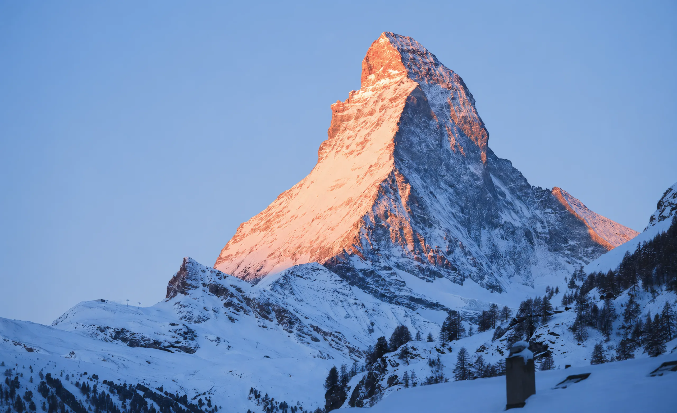 Alpenglow on a snow-covered mountain peak at dawn